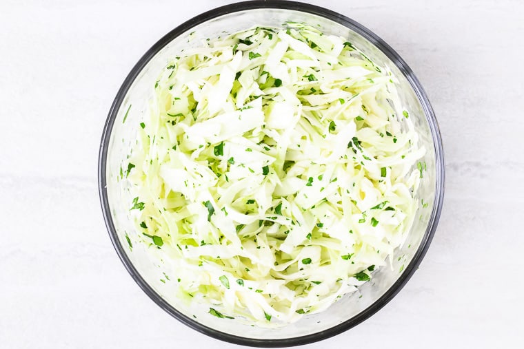 Cabbage slaw in a glass bowl over a white background