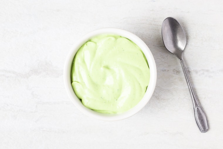 Avocado cilantro lime crema in a gray bowl with a spoon next to it on a white background