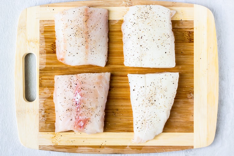 4 cod fillets on a wood cutting board with salt and pepper on them