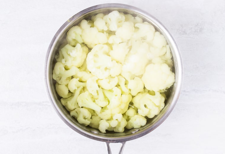 Boiled cauliflower in a silver pot over a white background