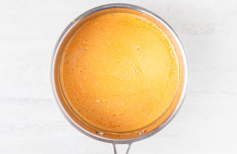 Cheese sauce in a silver pan over a white background