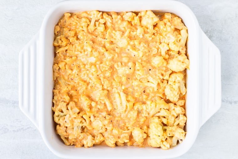 Cauliflower in cheese sauce in a square, white baking dish over a white background