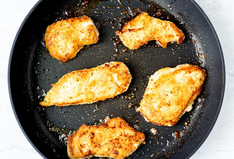 Cooked breaded chicken pieces in a skillet over a white background