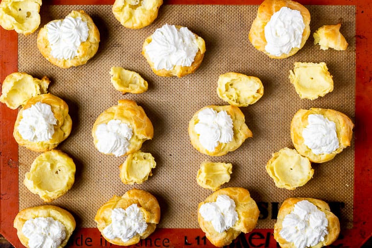 Cream puff shells filled with lemon cream with the tops off sitting next to them on a silpat mat
