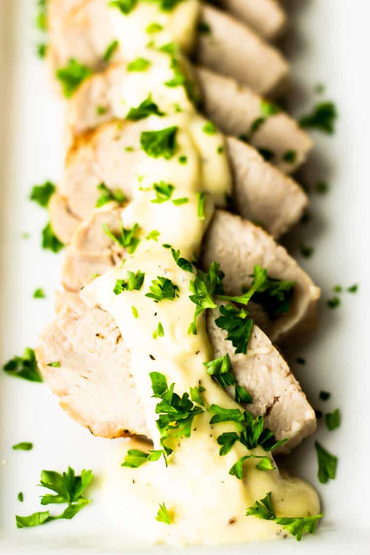 Close up of slices of pork loin topped with parmesan peppercorn sauce and fresh parsley on a white plate
