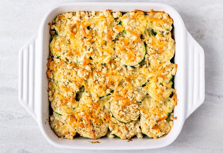 A Baked Zucchini Gratin with almond flour crumbs in a white casserole dish over a white background