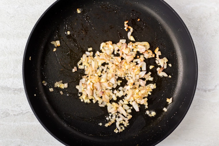 Shallot and garlic cooking in a black skillet over a white background