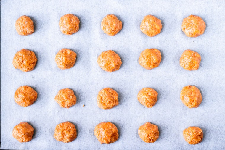 Buffalo chicken meatballs on a parchment paper lined baking sheet before cooking