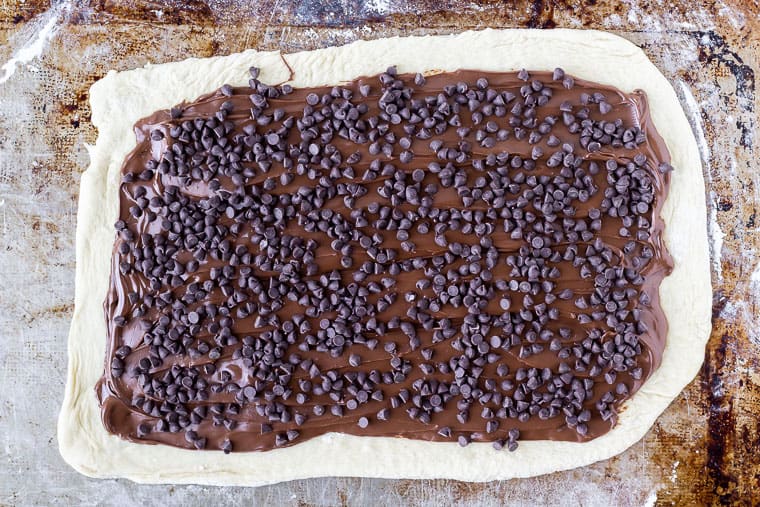 Pizza dough on a baking sheet topped with nutella and mini chocolate chips