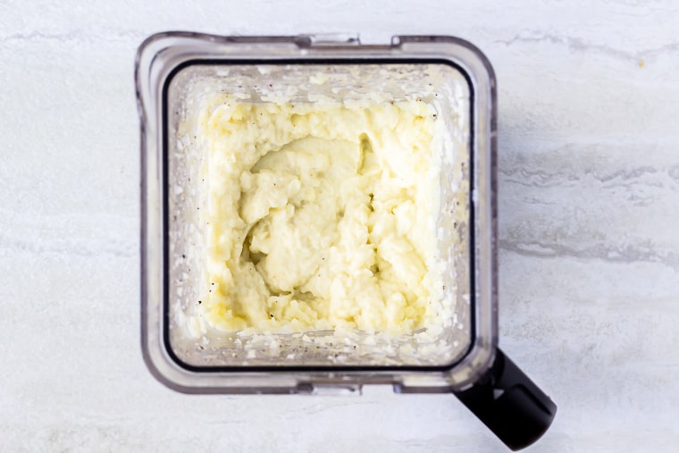 Mashed cauliflower in a blender over a white background