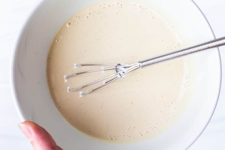 Caesar salad dressing in a white bowl with a small whisk