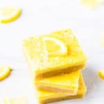 3 keto lemon bars stacked on top of each other with a lemon slice on top and a few more around them