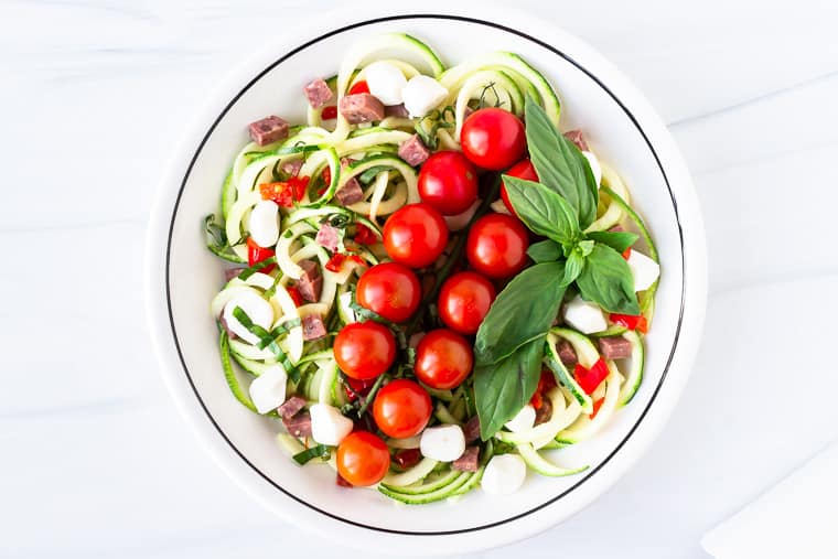 A zoodle pasta salad in a white bowl over a white background