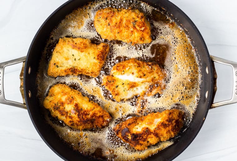 Cod fish fillets frying in oil in a skillet over a white background