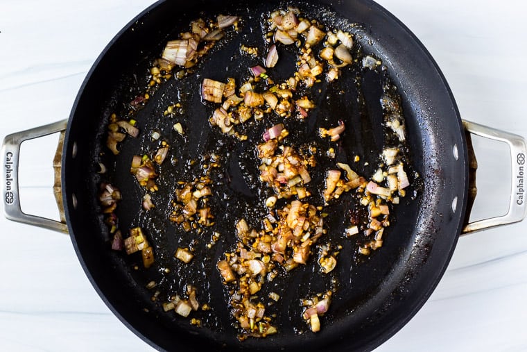 Garlic and shallot cooking in a black skillet over a white background