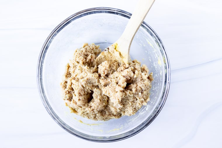 Ground chicken mixture in a glass bowl with a wood spoon over a white background