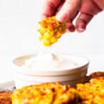 A corn fritter being dipped into sour cream.