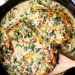 Keto Chicken Florentine in a cast iron skillet with a wood spatula lifting up a piece of chicken