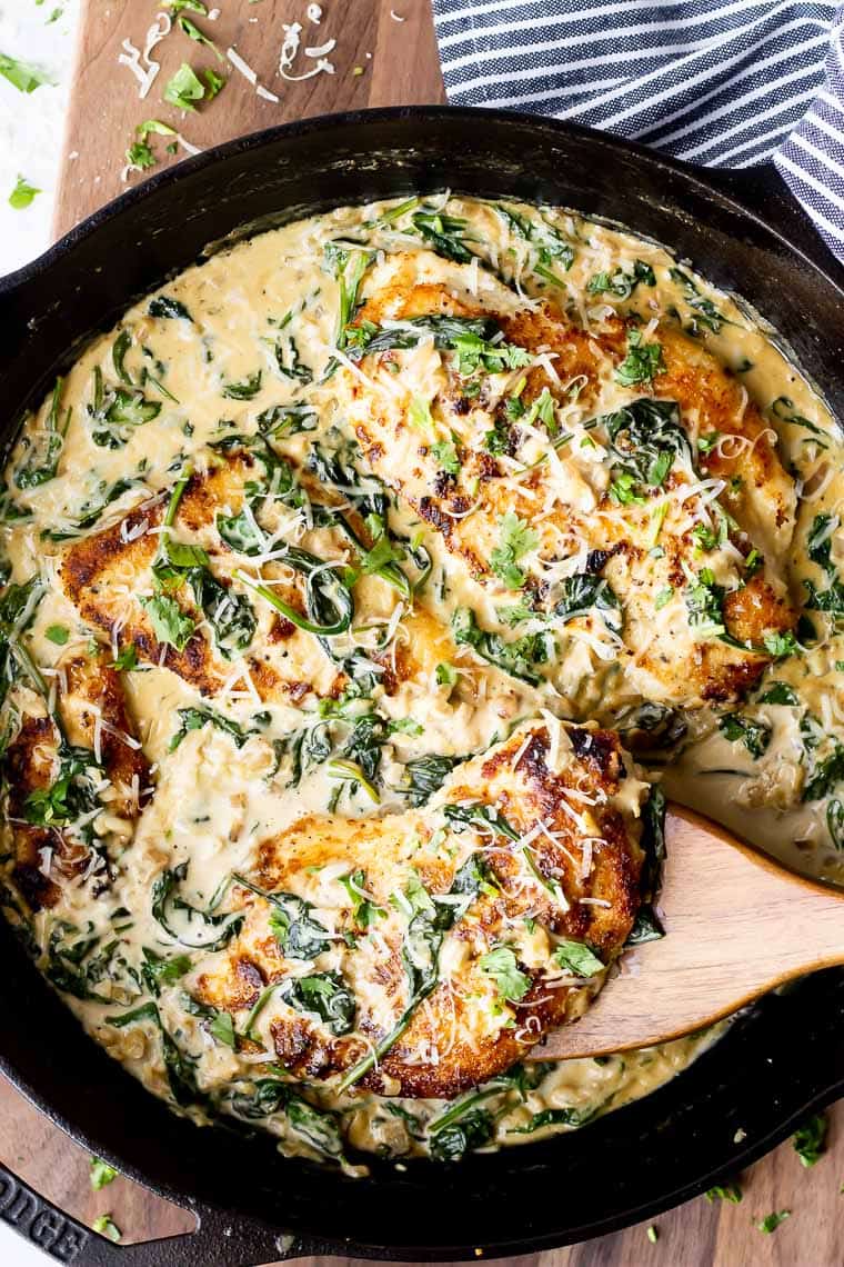 Keto Chicken Florentine in a cast iron skillet with a wood spatula lifting up a piece of chicken