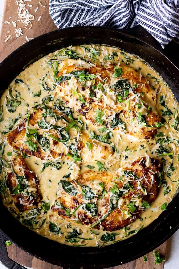Overhead of Keto Chicken Florentine in a cast iron skillet over a wood board with a blue and white striped towel around the handle and cheese scattered around