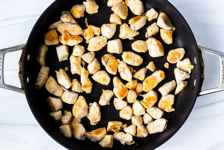 Chunks of chicken cooking in a black skillet