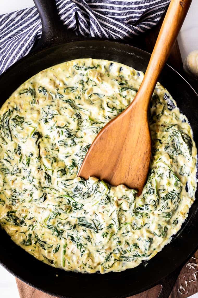 Overhead Keto Creamed Spinach with a wood turner on a wood board with a blue and white towel in the background
