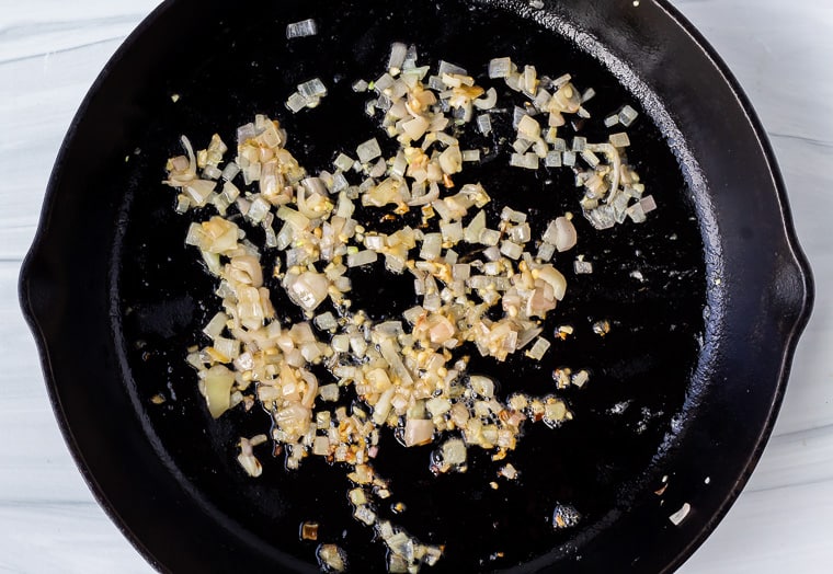 Minced shallot and garlic cooking in a black cast iron skillet