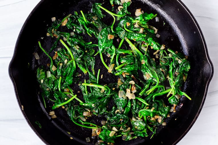 Cooked spinach with shallots and garlic in a black cast iron pan