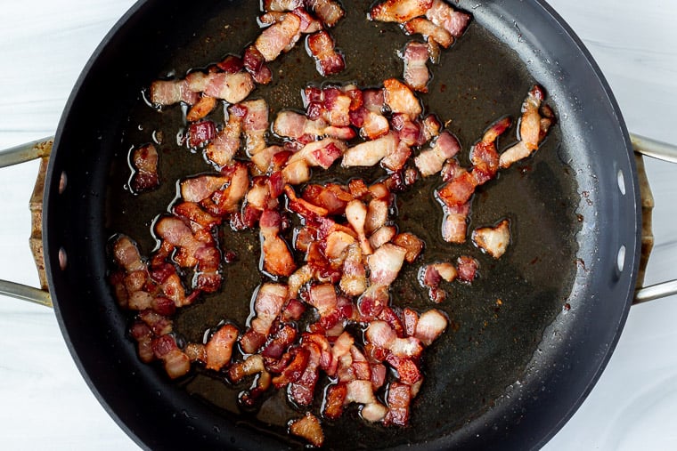 Diced bacon cooking in a black skillet