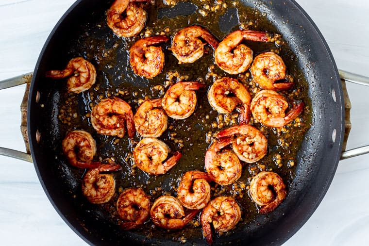 Cajun shrimp cooked in bacon grease in a skillet over a white background