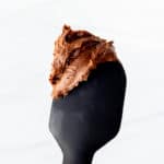 Homemade chocolate buttercream frosting on the tip of a spatula over a white background