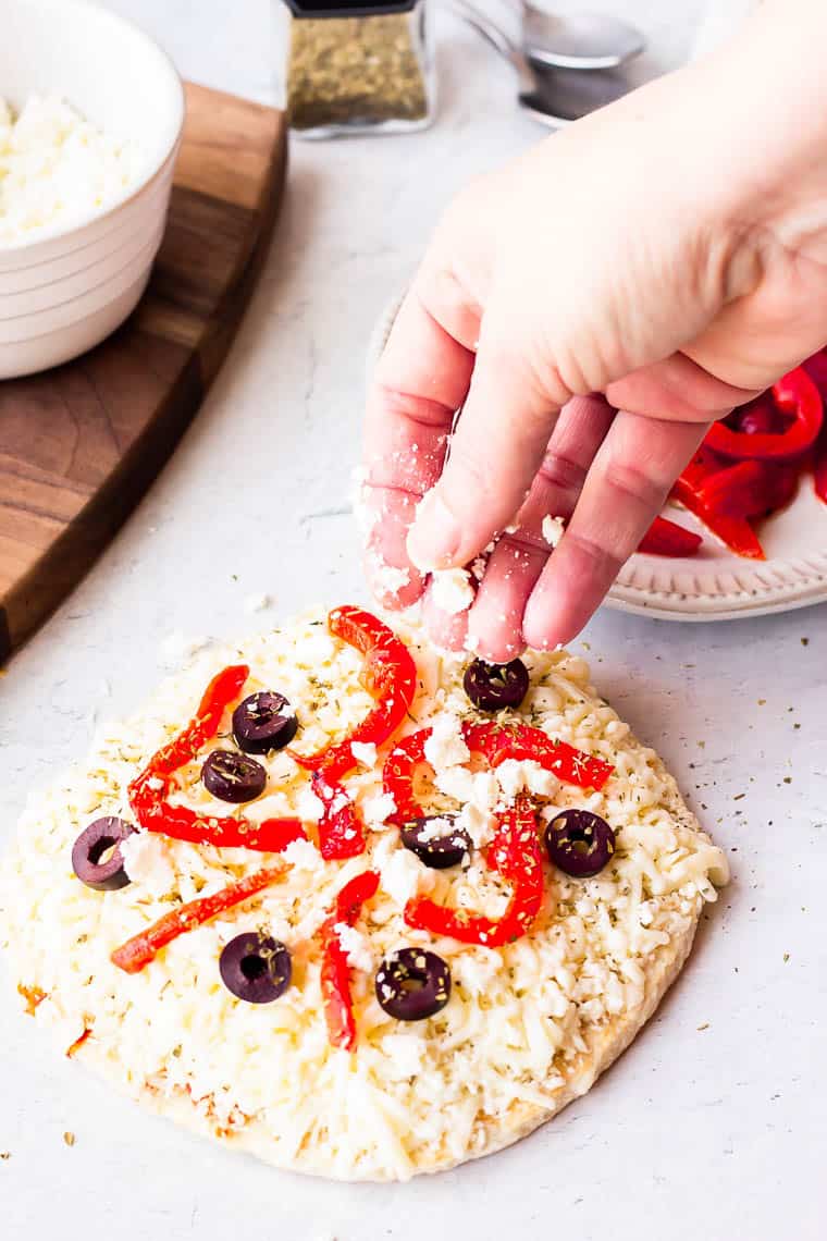 Sprinkling feta cheese on a greek pizza with other ingredients in the background