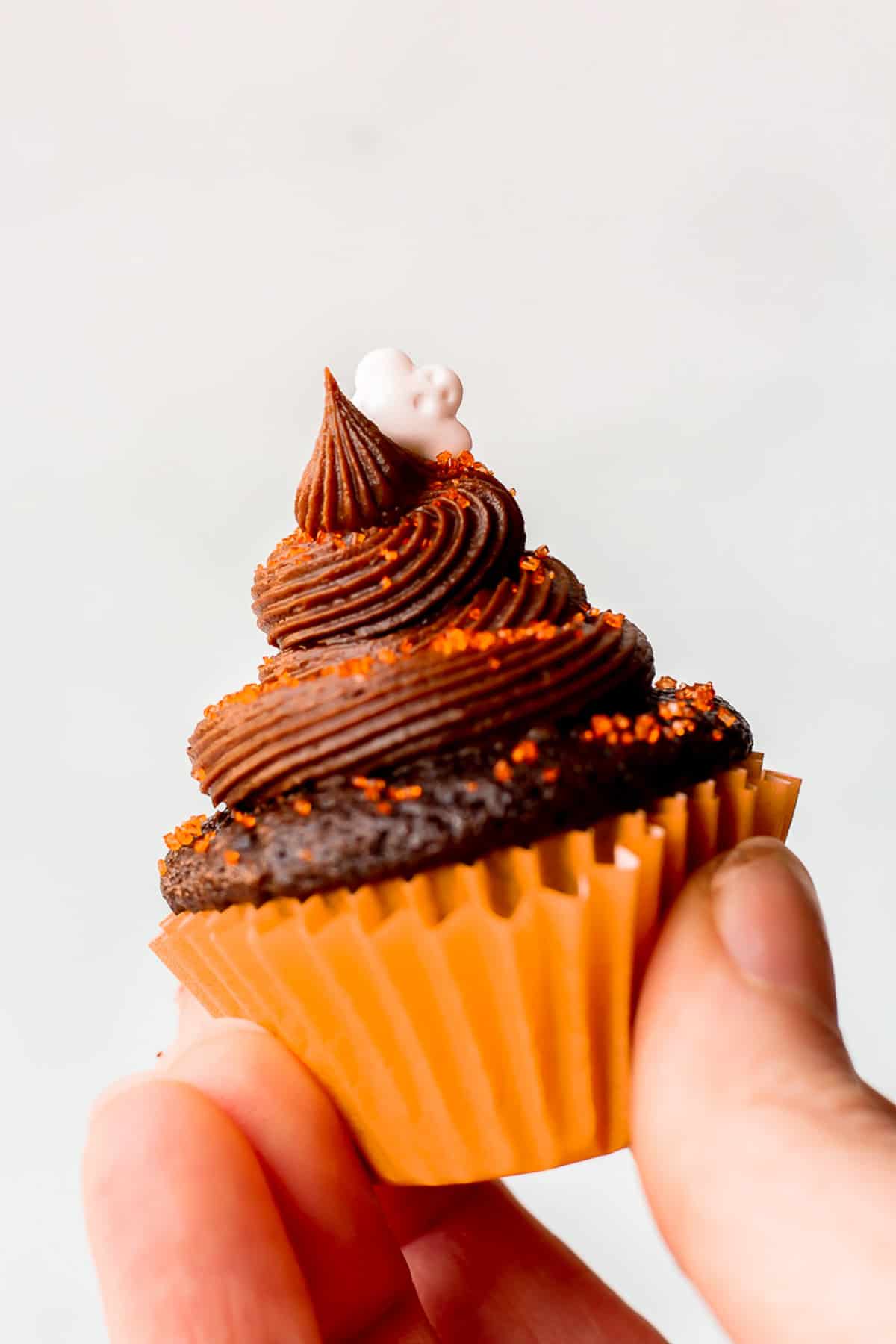 Hand holding up a single mini chocolate halloween cupcake with a white background