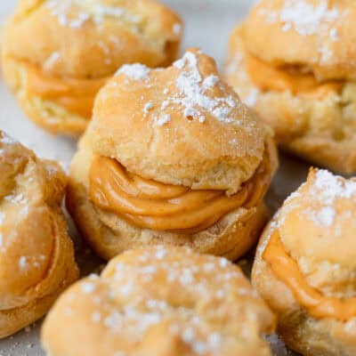Close up of a pumpkin spice cream puff surrounded by more cream puffs.