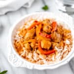 Coconut curry chicken with rice and peppers in a white bowl on a light background.