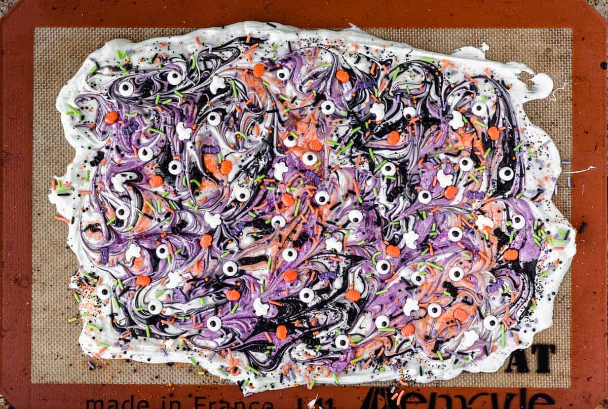 White chocolate halloween candy bark with swirls of black, orange, and purple and different halloween sprinkles and candies all over the top of it