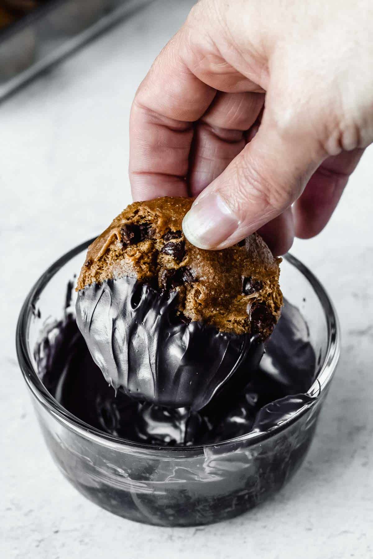 A hand dipping a cookie into melted black candy melts in a glass bowl