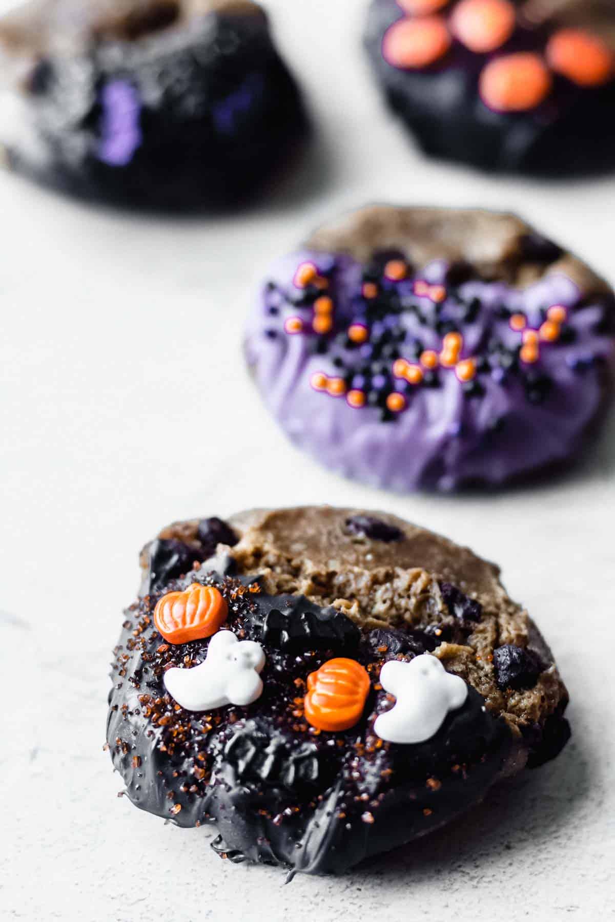 Chocolate chip cookies dipped in melted candy and decorated with Halloween sprinkles on a white background