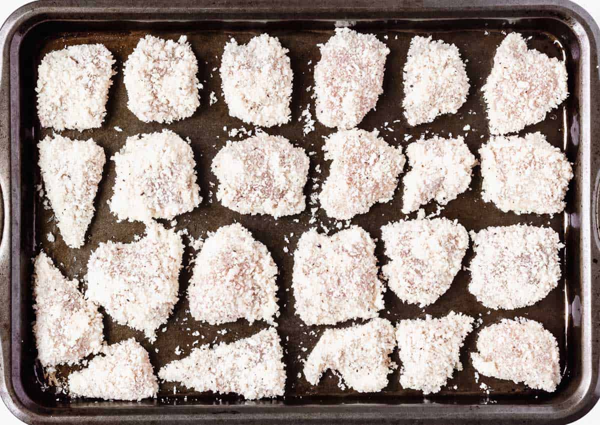 Homemade chicken nuggets breaded on a baking sheet before cooking.