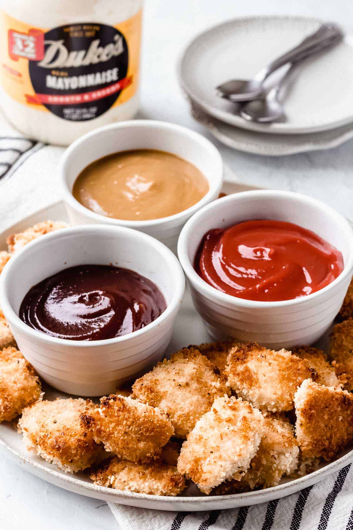 A plate of homemade chicken nuggets and dipping sauce with small plates, spoons, and Duke's mayonnaise in the background