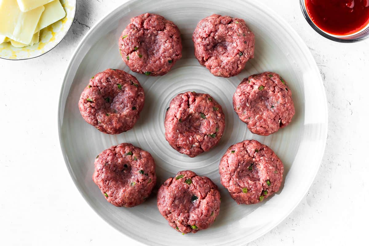 8 beef slider patties on a plate on a white background