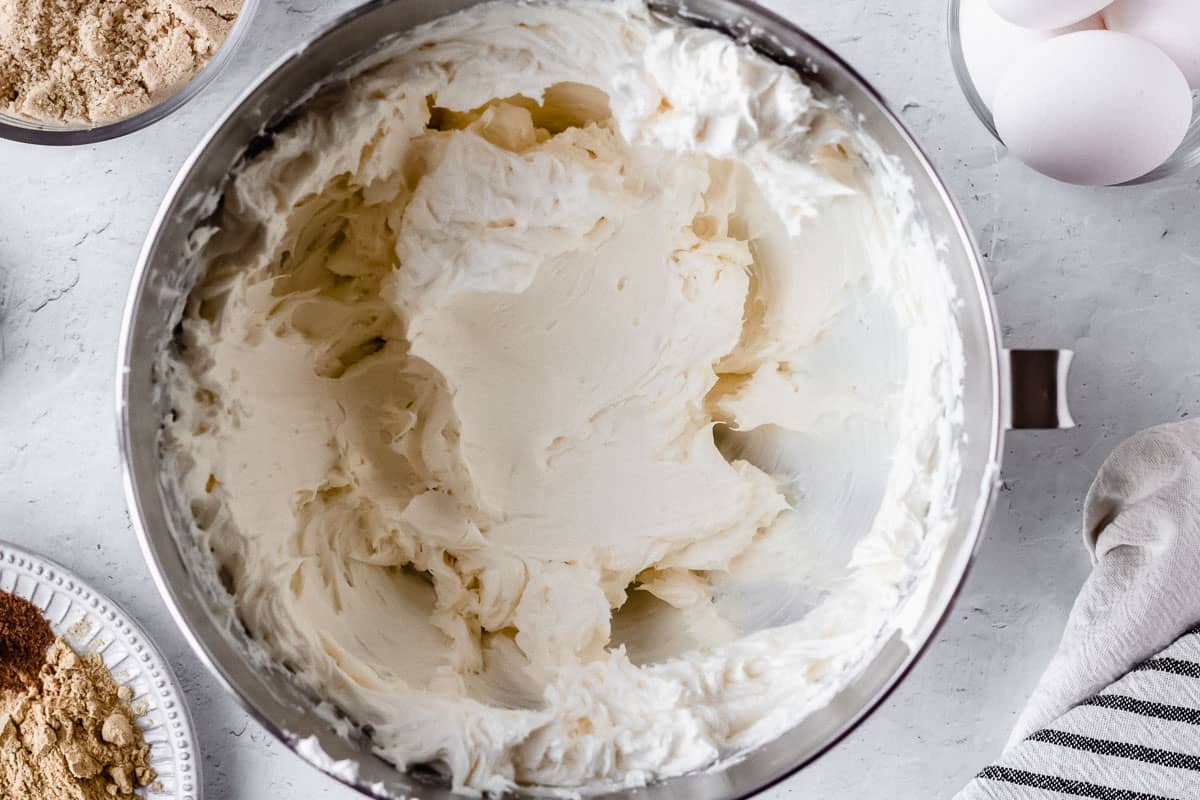 Cream cheese beat until fluffy in a silver mixing bowl with other ingredients around it