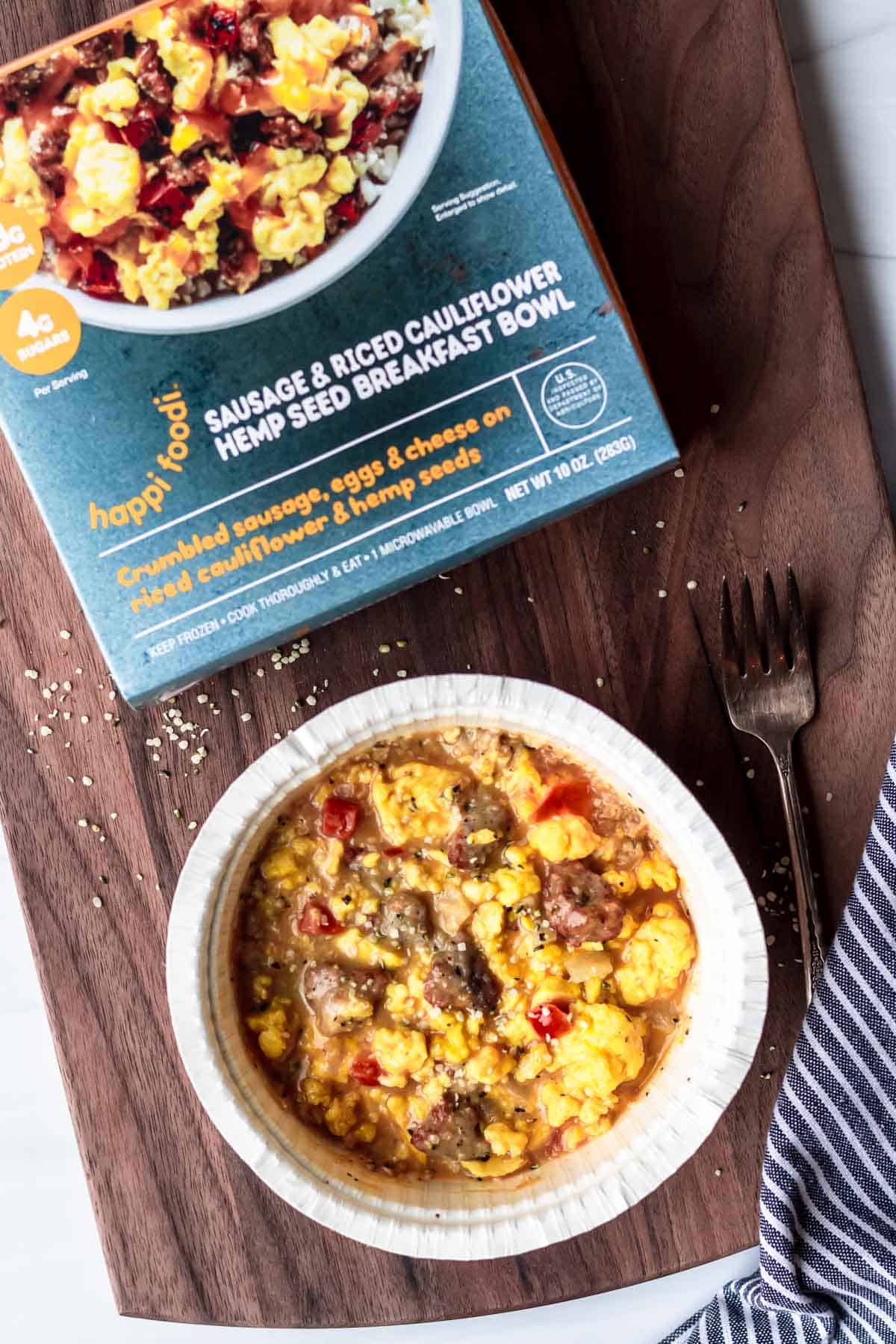 Sausage & Rice Cauliflower Hemp Seed Breakfast Bowl packaging and cooked meal on a wood background with a napkin and fork