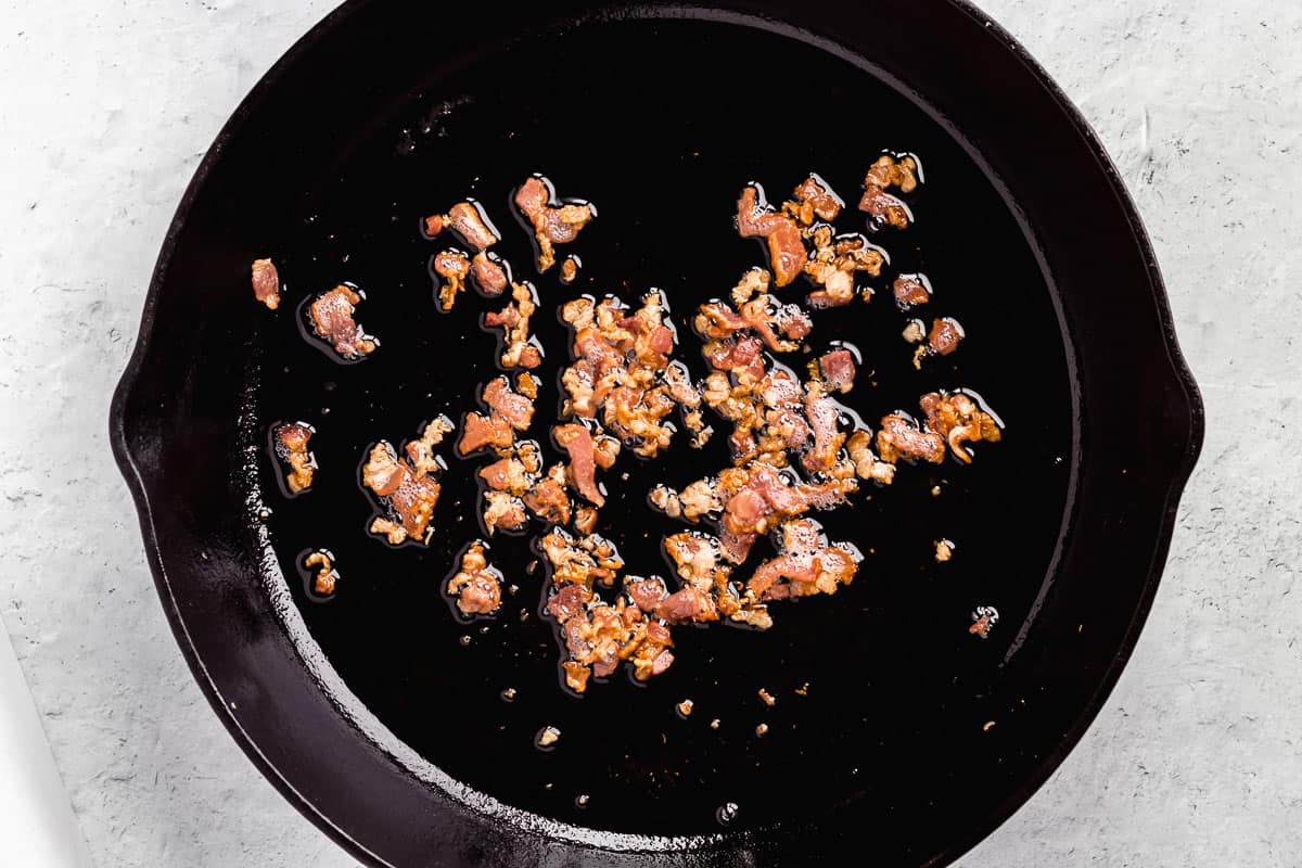 Diced bacon cooking in a cast iron skillet