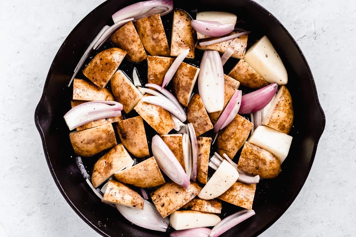 Potato wedges and shallots in a cast iron skillet