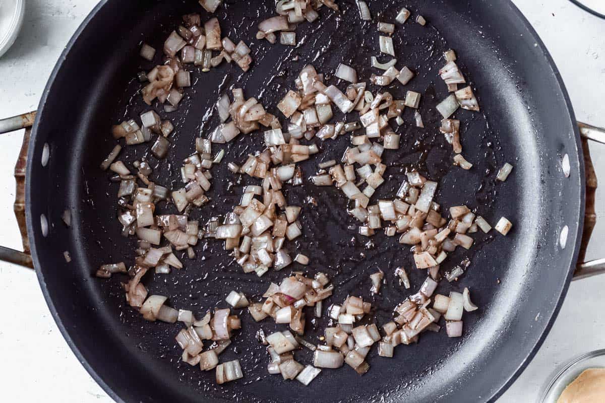 Garlic and shallots cooking in a black skillet over a white background