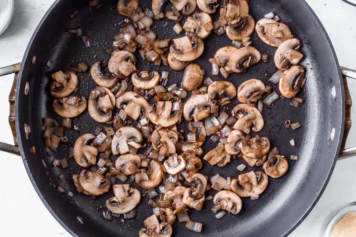 Slices of mushrooms cooking in a black skillet over a white background