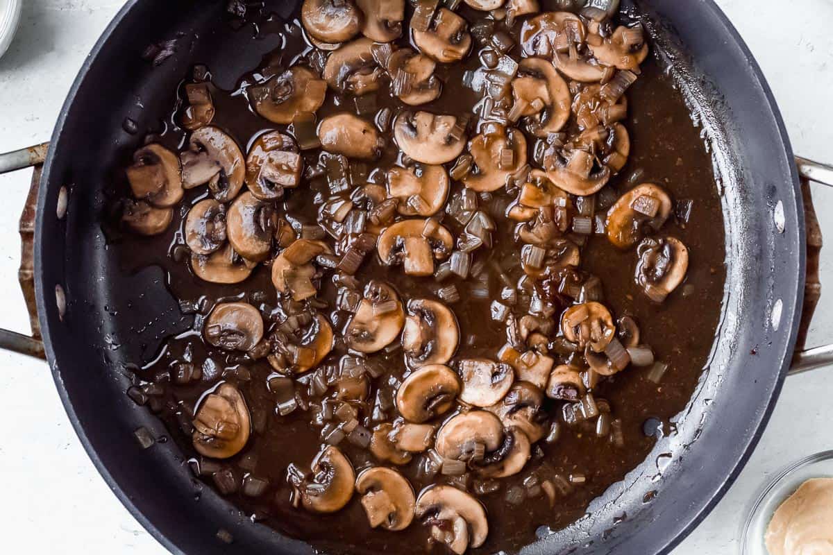 Mushrooms, shallots, garlic, and brown sauce in a black skillet over a white background