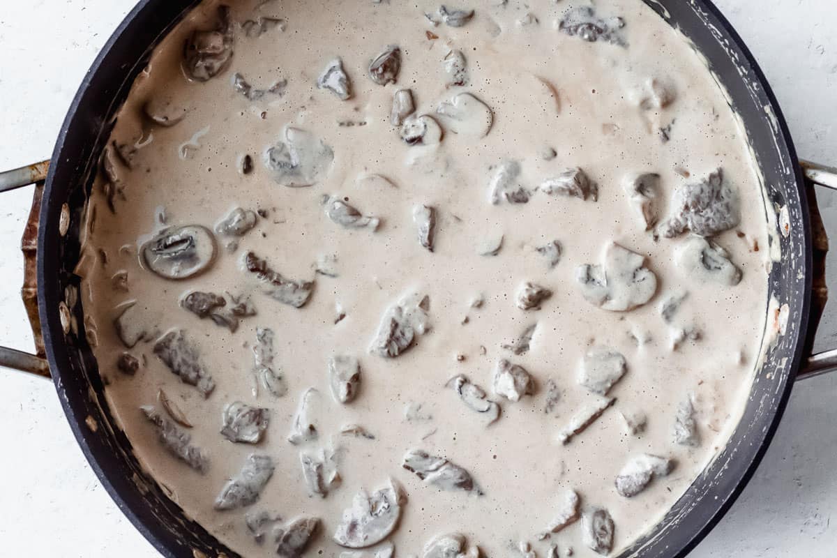 Beef and mushrooms in a cream sauce in a black pan over a white background