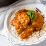Butter chicken on a bed of white rice in a white bowl over a white background